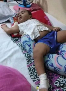 A little boy is lying on a hospital bed with an IV cannula in his right leg.
